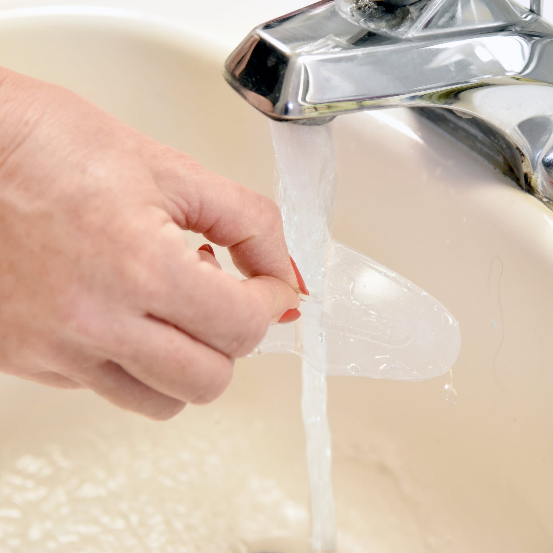 Hand holding a Somnoseal under a running faucet in a sink.